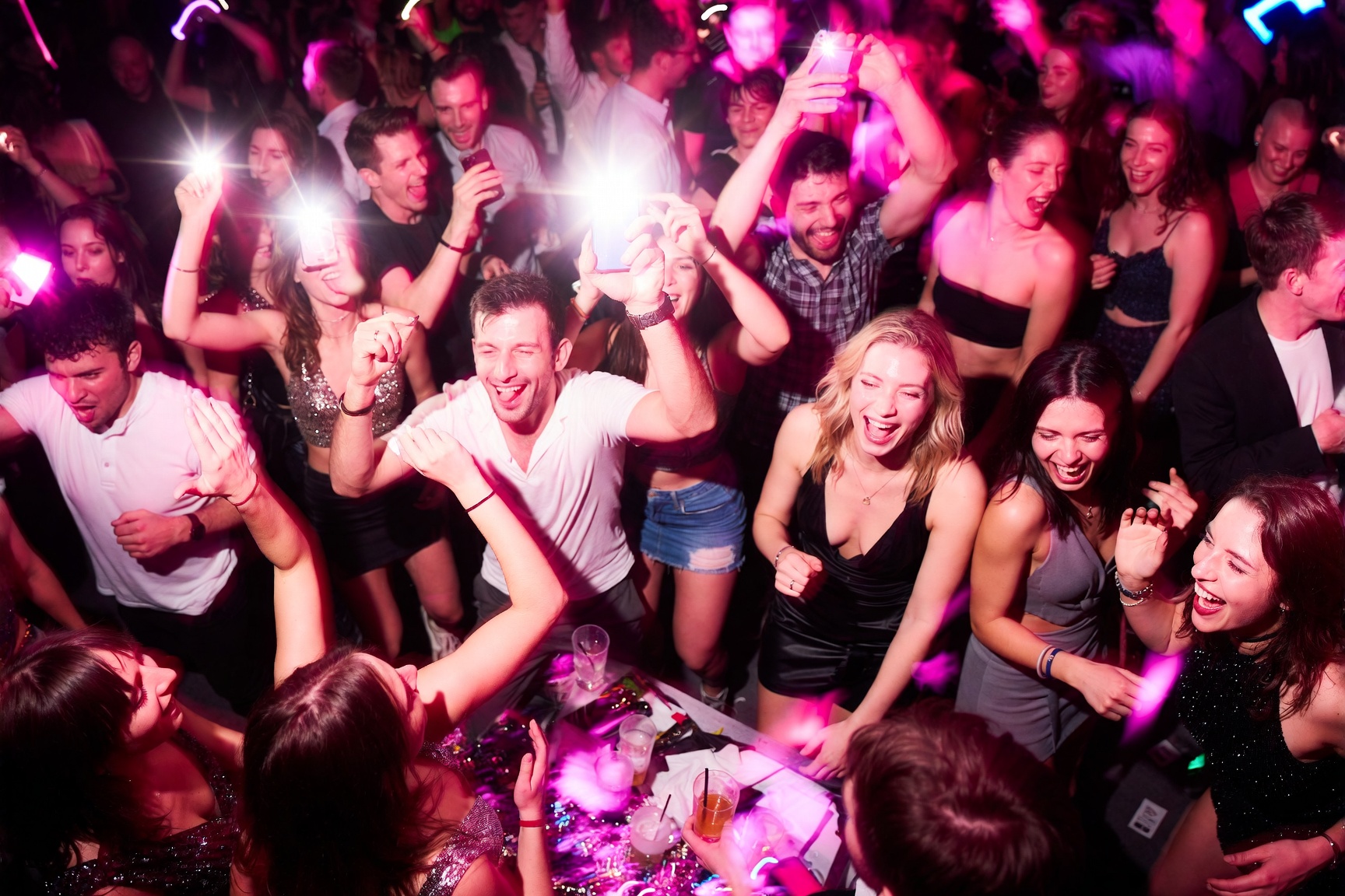 A packed dance floor under pink party lights